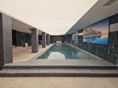Moderner Indoor-Pool mit dunklen Steinböden und großen Landschaftsbildern an der Wand.