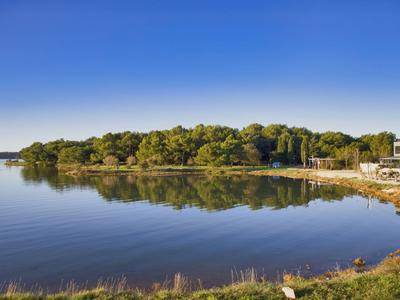 Ruhevolle Küstenlandschaft mit klarem Wasser, bewaldeter Halbinsel und Ferienhäusern unter blauem Himmel.