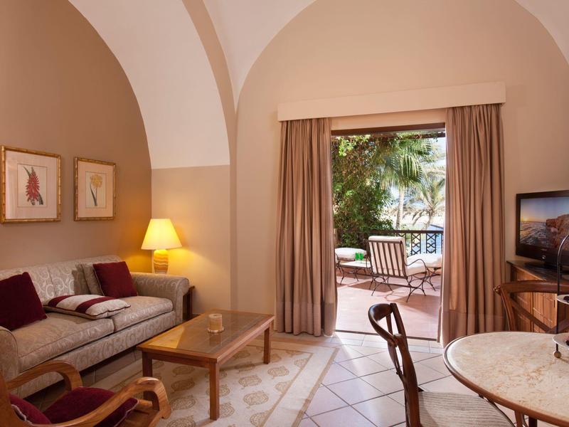 Gemütliches Wohnzimmer mit gewölbter Decke, Sofa, Tisch, Lampe und Blick auf Terrasse mit Pflanzen.