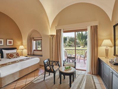 Helles Hotelzimmer mit Doppelbett, Sitzbereich und Terrasse mit Blick auf Garten.