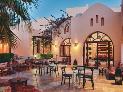 Cour intérieure d'un hôtel avec tables, chaises et arches décoratives sous une lumière chaleureuse du soir.