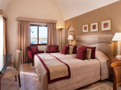 Chambre d'hôtel chaleureuse avec lit double, fauteuils rouges et vue sur mer.