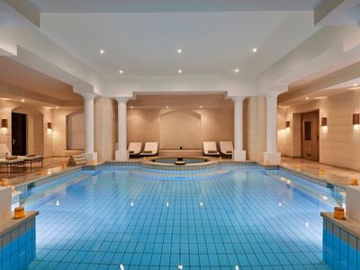 Piscina interior con columnas, tumbonas modernas y luz cálida en un hotel.