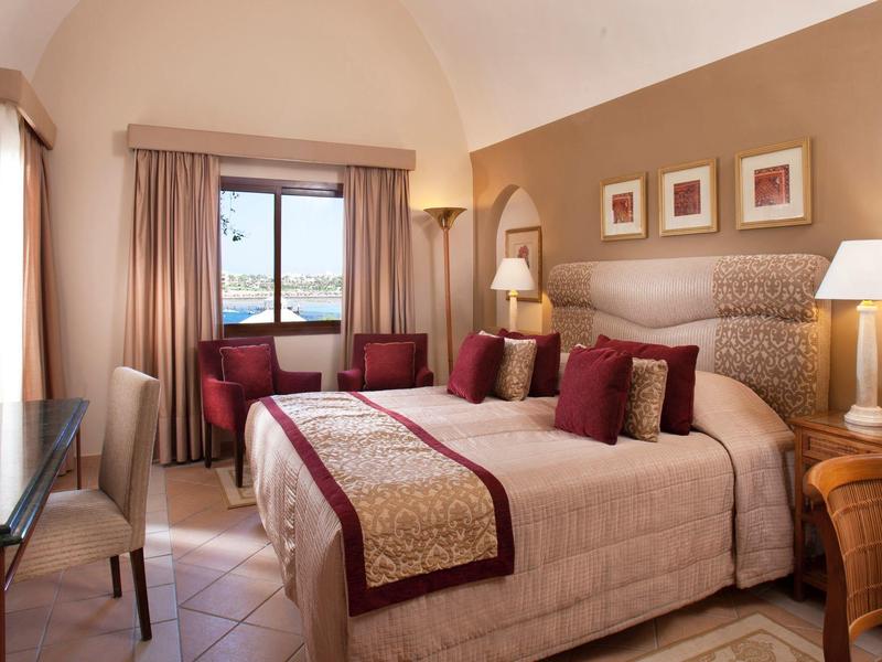 Cómoda habitación de hotel con cama doble, sillas, escritorio y vista al mar.