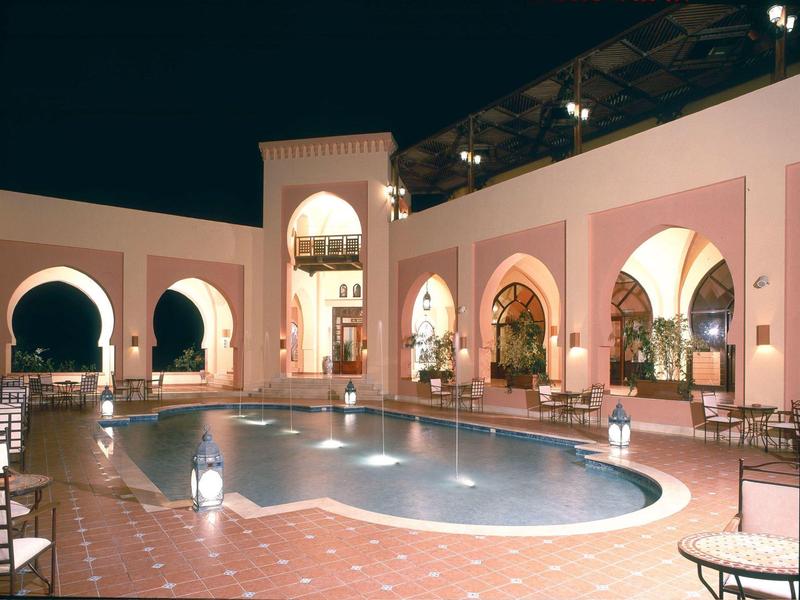 Cortile di hotel in stile marocchino con piscina illuminata e lanterne di notte.