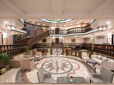 Elegancka lobby hotelowa z marmurową podłogą, dwiema klatkami schodowymi i stylowymi miejscami do siedzenia.