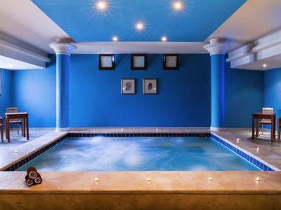 Piscina interior con paredes azules, columnas blancas y efecto de agua en el hotel.