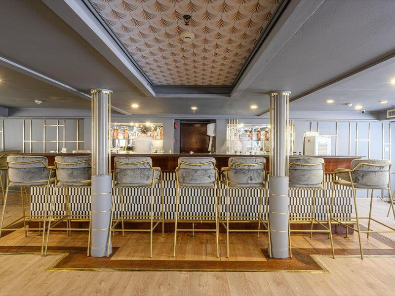 Moderní bar se zlatými stoličkami, zdobeným stropem a tlumeným osvětlením.