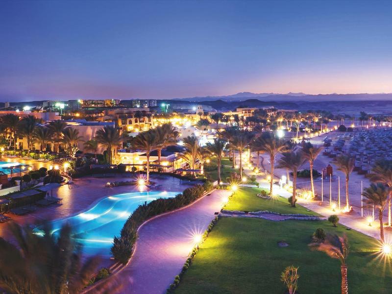 Night view of a lit hotel pool and adjacent green areas by the coast.