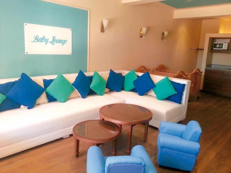 Hotelowy kącik wypoczynkowy z dużą białą kanapą, kolorowymi poduszkami i drewnianymi stolikami.