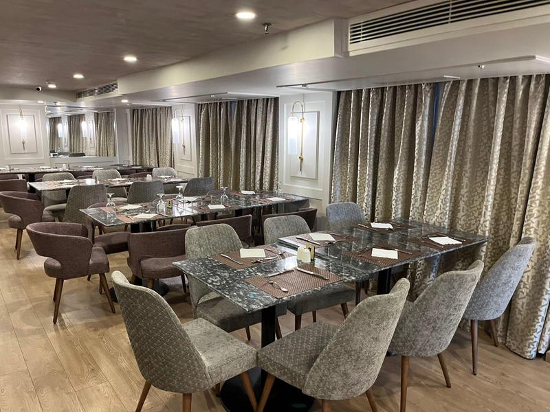 Moderne eetruimte in hotel met beklede stoelen, gedekte tafels en grote gordijnen langs de muur.