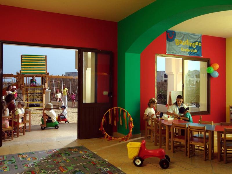 Zona de juegos interior y exterior en un hotel con niños jugando y mobiliario colorido.