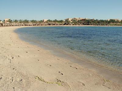 Plage de sable doré calme avec eau claire et ligne d'hôtels en arrière-plan.