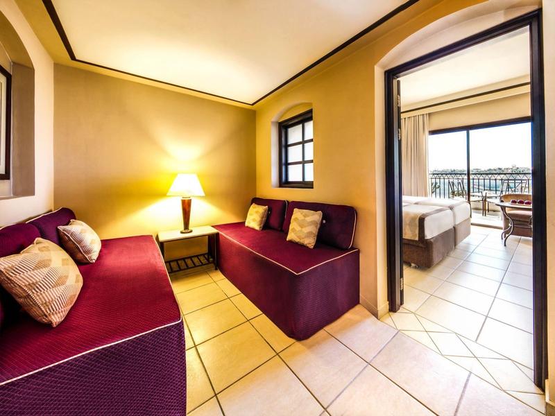 Salon avec canapés rouges et lampe, vue sur une chambre lumineuse avec balcon.