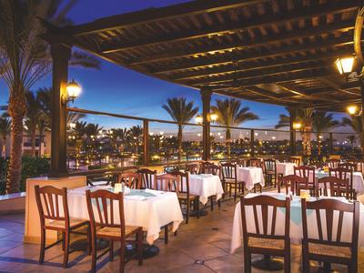 Terraza de restaurante por la tarde con mesas preparadas y vista de la ciudad iluminada y palmeras.