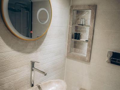 Kleines Bad mit ovalem Waschbecken, rundem Spiegel und eingebauten Regal mit Badezimmerartikeln.