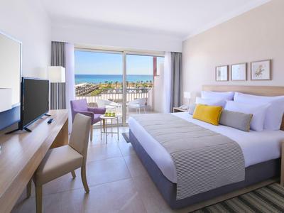 Moderne hotelkamer met tweepersoonsbed en uitzicht op zee vanaf het balkon.