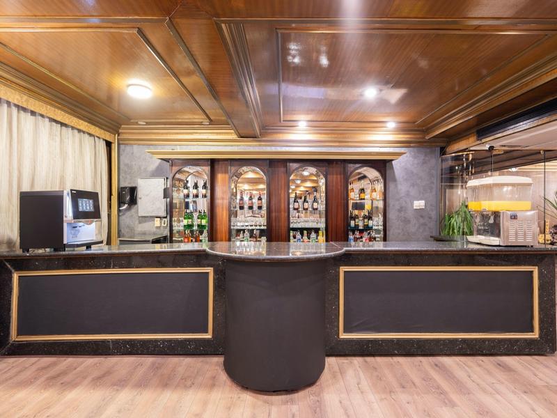 Área moderna de bar de hotel con techo de madera, barra larga y estantes decorativos de vino al fondo.