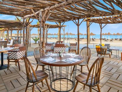 Ristorante all'aperto sulla spiaggia con mobili in legno e vista sul mare con sole.