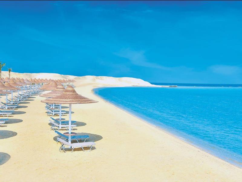 Piaszczysta plaża z leżakami ustawionymi pod jasnym niebieskim niebem.