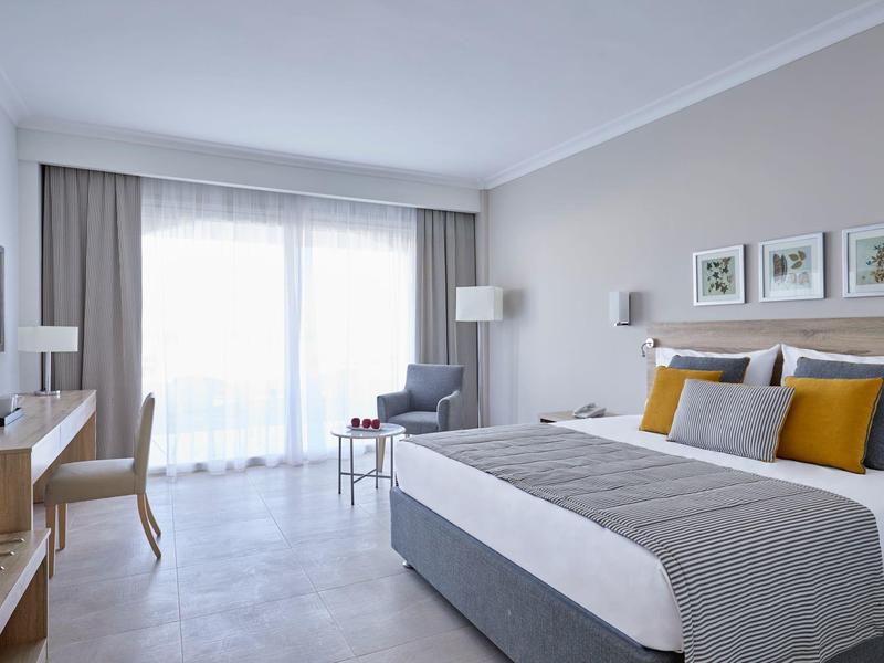 Habitación de hotel moderna con cama doble, zona de asiento y ventana grande con cortinas.