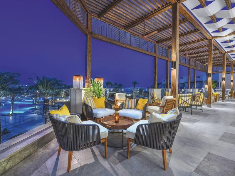 Cómodas áreas al aire libre con muebles acolchados y vista a una piscina iluminada por la noche en el hotel.