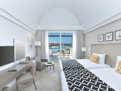 Habitación de hotel luminosa con vista al mar, cama doble, escritorio y decoración moderna.