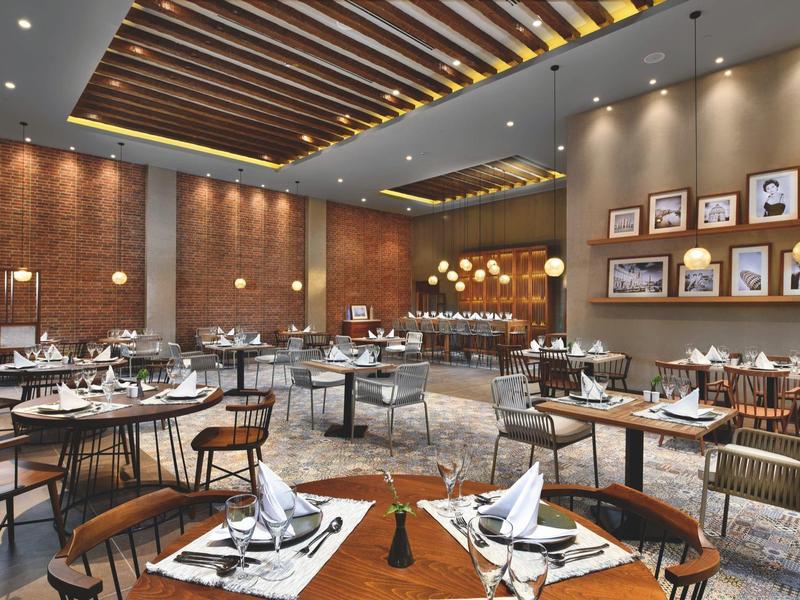 Ristorante elegante con tavoli apparecchiati, sedie in legno, muri in mattoni e illuminazione calda.