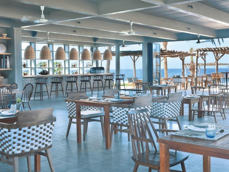 Ampio ristorante luminoso con vista mare e arredi in legno e rattan.