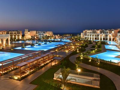 Luxuriöse Nachtansicht eines beleuchteten Poolbereichs in einem Resort am Meer.