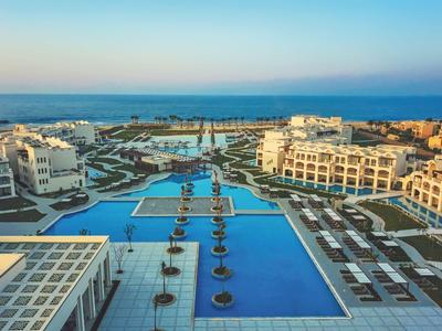 Große Hotelanlage mit mehreren Pools und Meerblick bei klarem Himmel.
