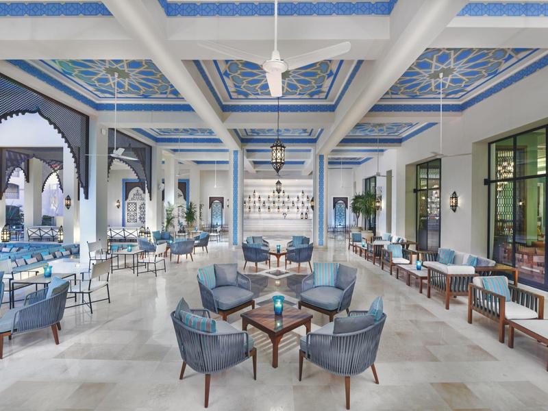 Ampia sala d'hotel con pareti bianche, poltrone blu e decorazioni azzurre.