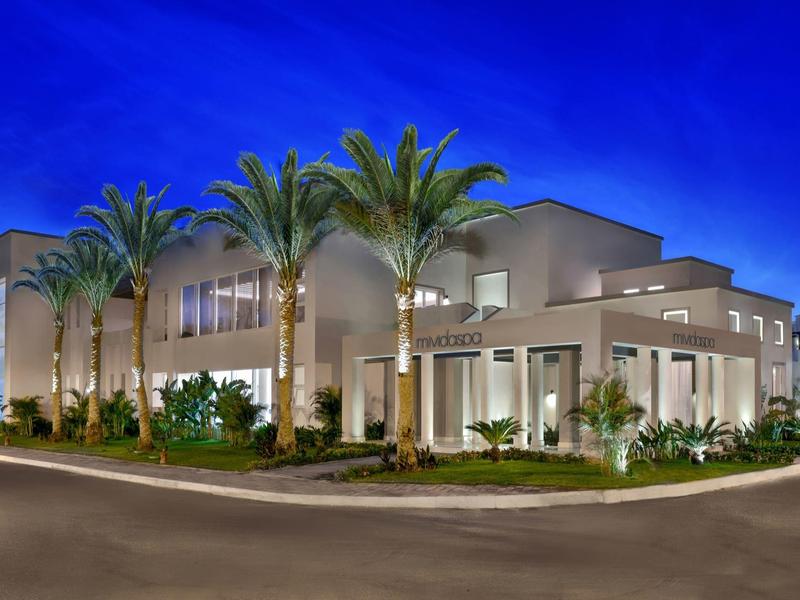 Hotel moderno illuminato di notte con palme davanti all'ingresso.