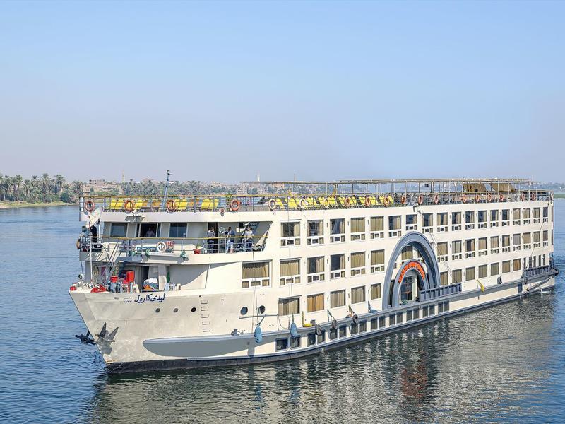 Großes weißes Passagierschiff mit mehreren Decks fährt auf ruhigem Fluss bei blauem Himmel.
