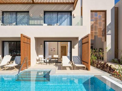 Modern villa with poolside lounge chairs and large wooden shutters open to the patio.