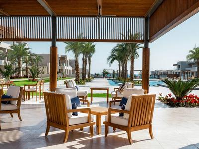 Terraza cubierta con sillas de madera y vistas a un jardín tropical y piscina en un resort.