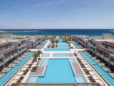 Complex de luxe avec plusieurs piscines et vue sur l'océan sous un ciel bleu clair.