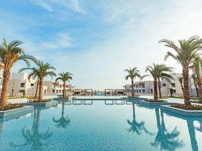 Piscine d'hôtel moderne avec palmiers et bungalows sous un ciel dégagé