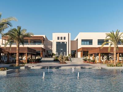 Complexe hôtelier moderne avec piscine, palmiers et terrasses ensoleillées sous un ciel bleu clair