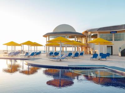 Hotelpool mit gelben Sonnenschirmen und blauen Liegestühlen bei Sonnenaufgang.