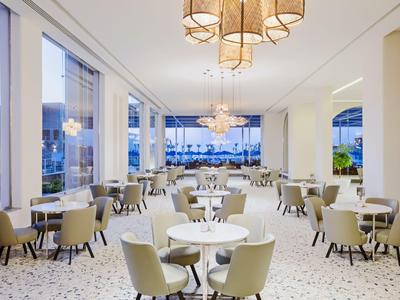 Helles, modernes Restaurant mit weißen Wänden, großen Fenstern und vielen Tischen mit Stühlen.