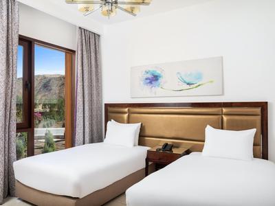 Hotelkamer met twee eenpersoonsbedden, een houten hoofdeinde en een raam met uitzicht op de bergen.