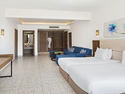 Ruime hotelkamer met twee bedden, blauwe bank en moderne inrichting met kunst en tv.