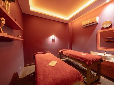 Gezellige massageruimte met twee bedden, warme verlichting en rode muren, ontworpen voor ontspanning.