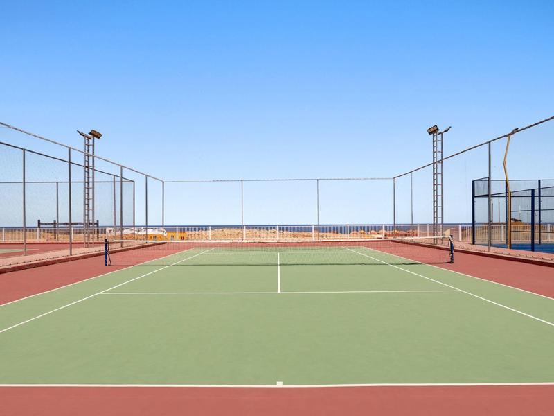 Leeg buitentennisbaan met heldere lucht en omheining eromheen.