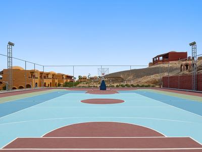 Campo da basket esterno vuoto con case e colline sullo sfondo sotto un cielo limpido