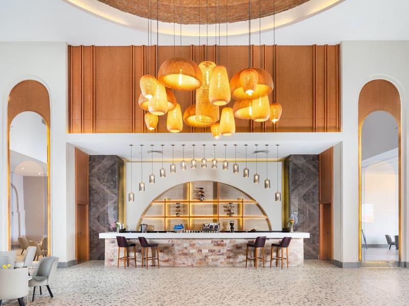 Recepción de hotel elegante con iluminación colgante y sillas frente al mostrador de mármol.