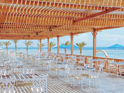 Ampia terrazza aperta con sedie bianche e tetto in legno con vista sul mare.