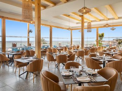Restaurant lumineux avec cadres en bois, chaises en cuir et vue sur la mer par de grandes fenêtres.