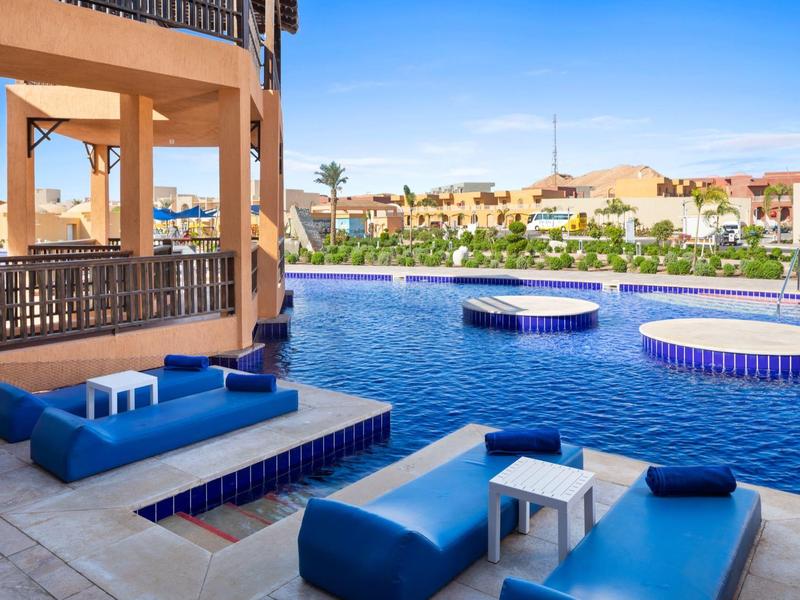 Terrasse avec fauteuils bleus au bord d'une piscine ronde dans un complexe hôtelier.